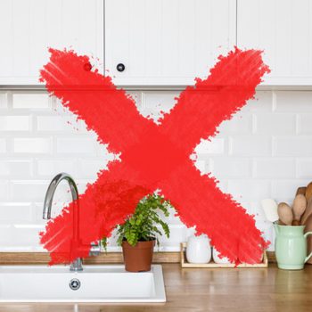 Red X marks a kitchen counter with a potted plant, sink, cutting boards, and utensils, against a white tiled backsplash.