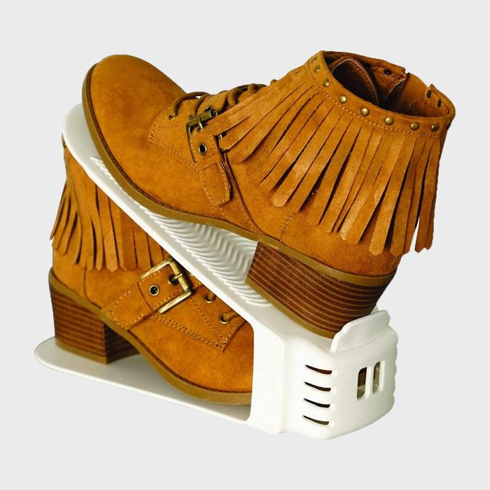 Fringed brown boots rest on a white plastic shoe organizer, stacked neatly in a minimalist setting.