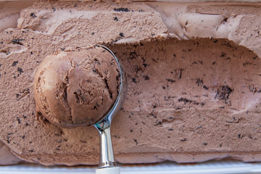 Chokolate ice cream Flat lay. Top view. Spoon for ice cream takes a little out of the package. Macking ball of ice cream. Space for text. Chokolate ice cream with pieces of chocolate.