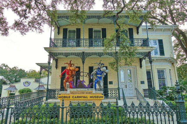 Statues of jesters stand on a porch, flanking the entrance of a historic building. Sign reads: "Mobile Carnival Museum, William & Emily Hearin."