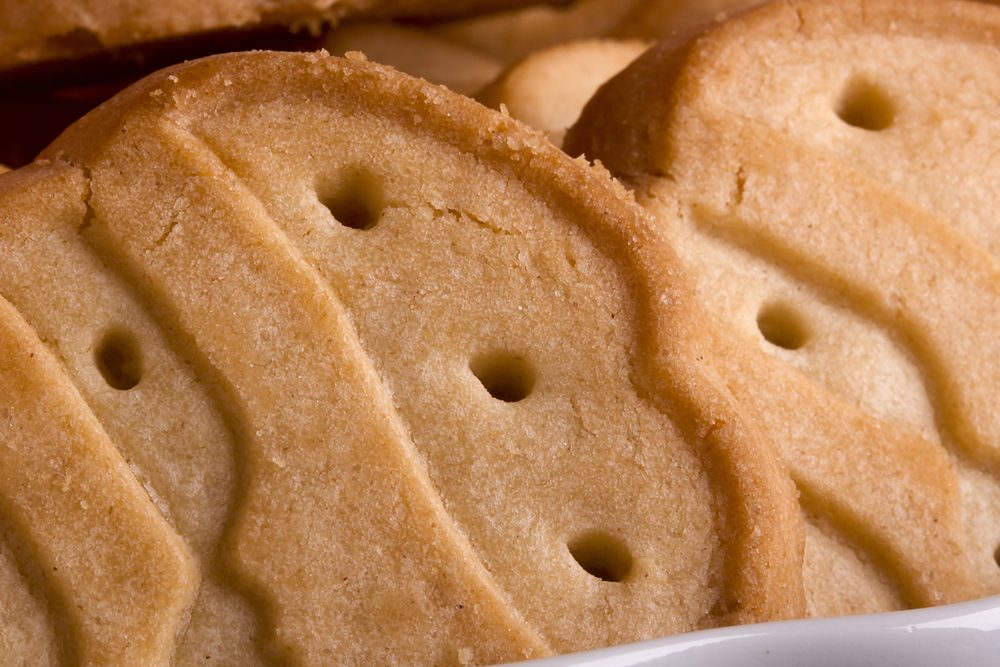 Cookies rest closely together, showcasing a wavy pattern and small holes, with a warm, golden-brown color.