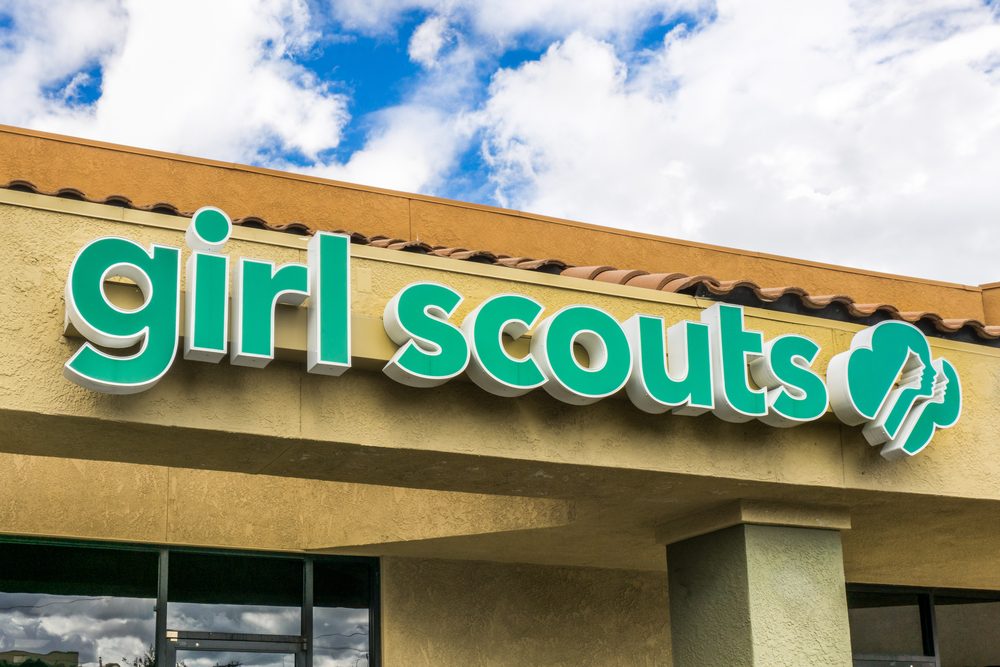 The "girl scouts" sign is displayed on a building's exterior, under a partly cloudy sky.
