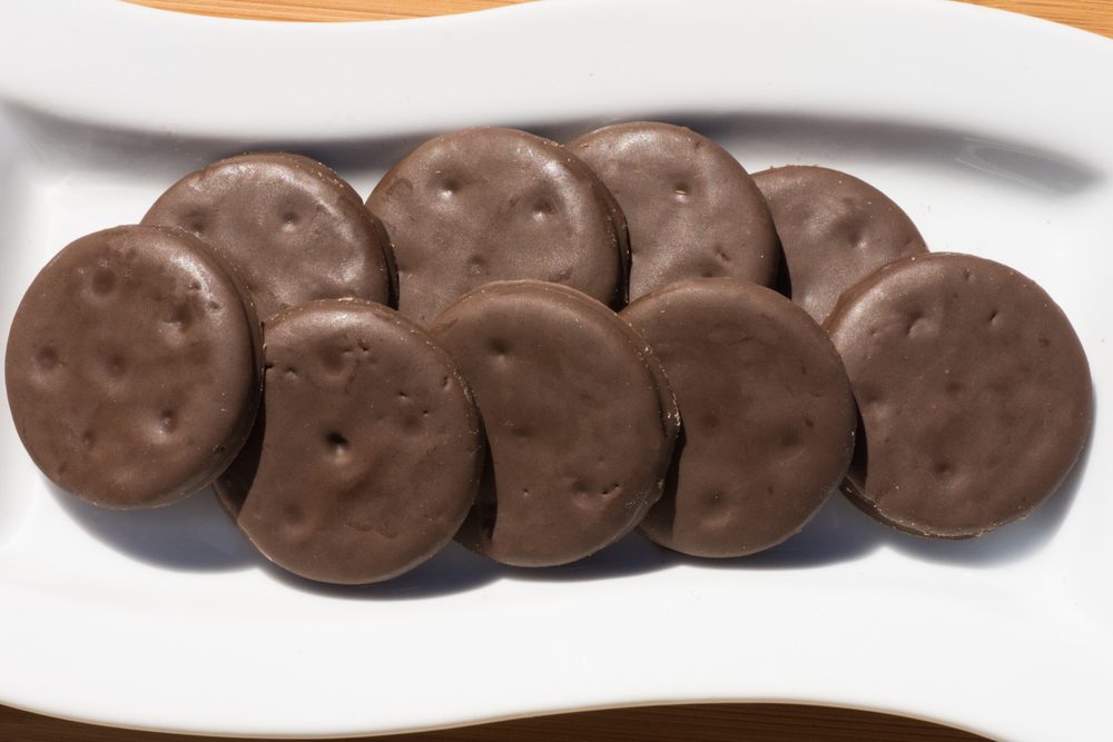 Cookies sit arranged on a white plate, covered in chocolate, on a wooden surface.
