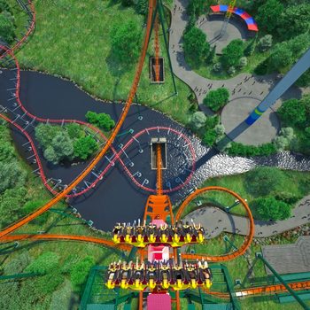 Roller coaster descends steeply over river; people ride with feet dangling. Lush greenery and pathways below, amusement park rides visible in background.