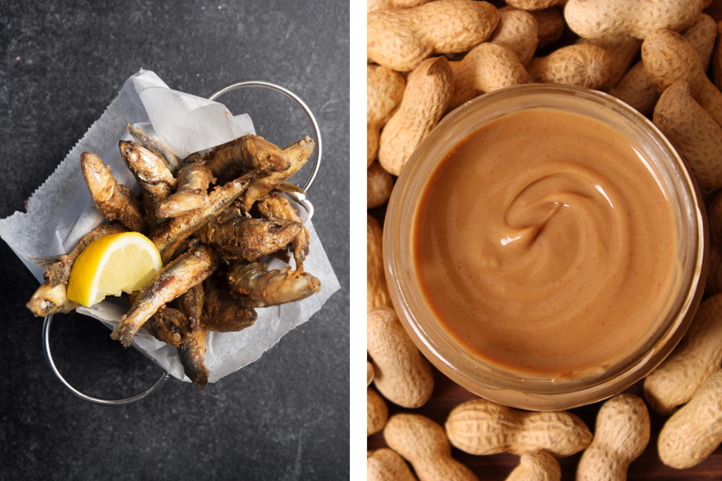 Fried fish lie in a basket with lemon on a dark surface; creamy peanut butter jar is surrounded by unshelled peanuts.