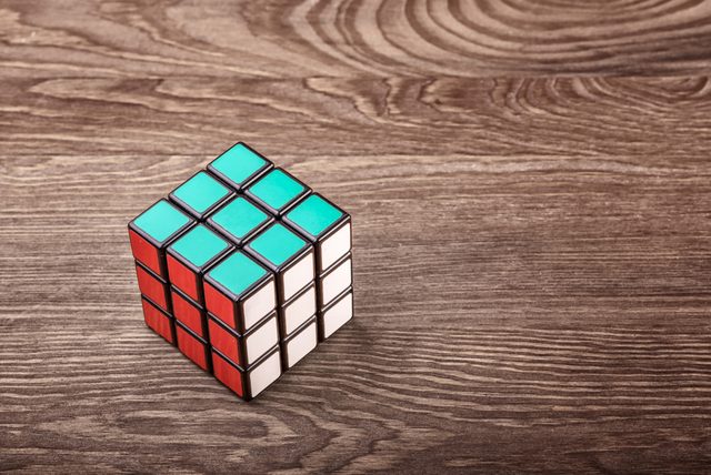Rubik's Cube sits unsolved on a textured wooden surface, showing green, red, and white faces.