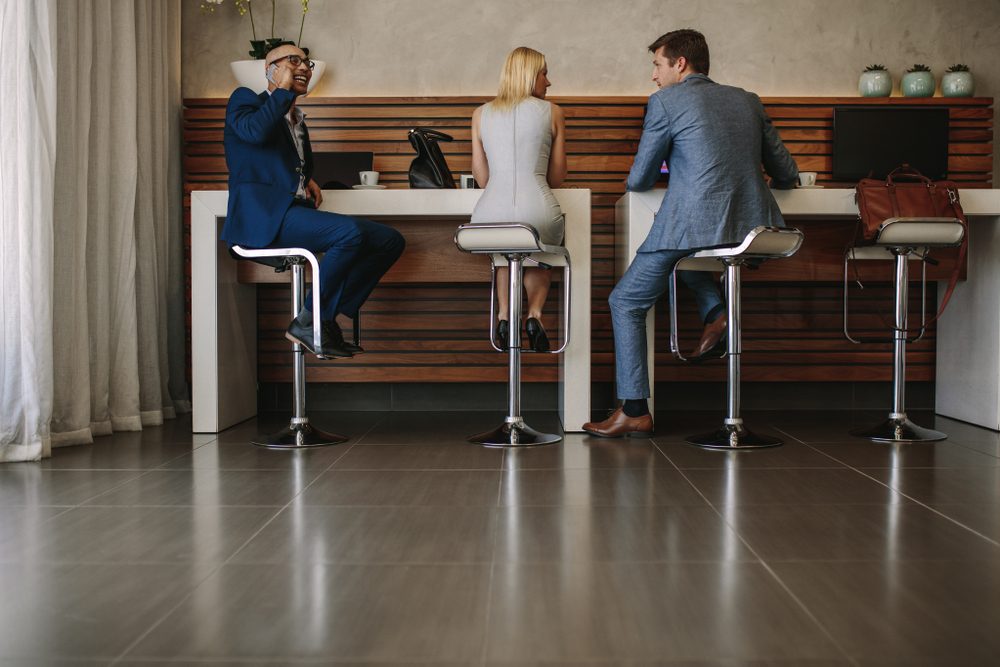 Airline passengers sitting at free internet service counter in airport. People at internet cafe inside airport terminal.
