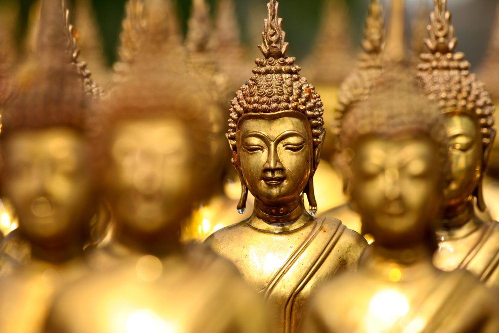 Golden Buddha statues, standing closely, creating a serene and harmonious pattern with soft lighting and blurred background in a tranquil setting.