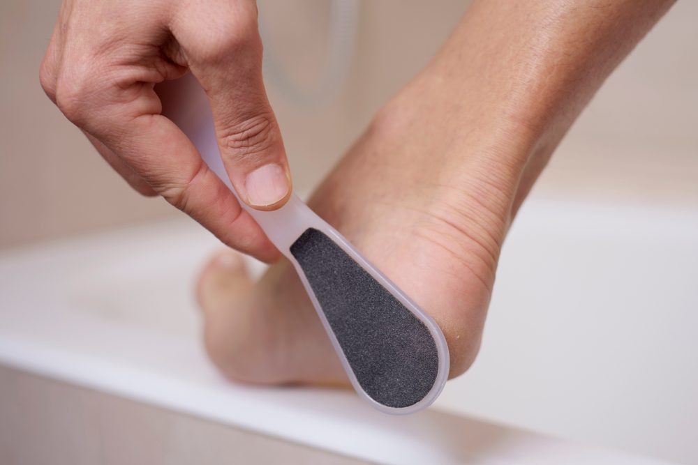 Hand uses a foot file on a heel, smoothing skin in a bathroom setting.