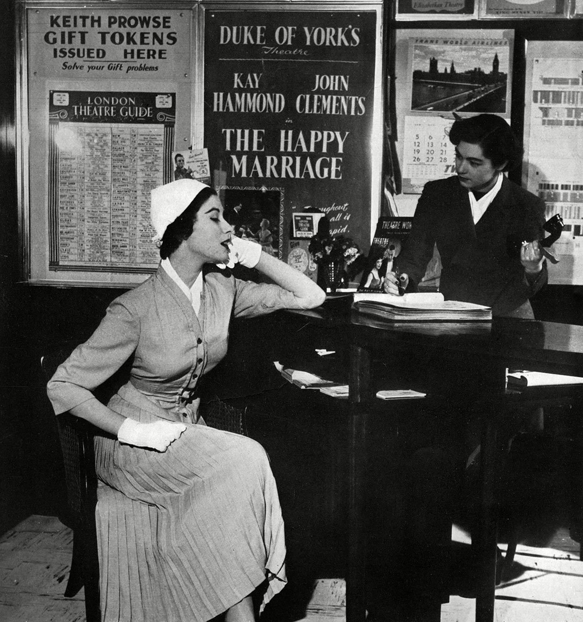 Historical Collection 170 A Stylishly Dressed Woman Books Tickets For the Theatre Wearing A Slim-fitting Featherweight Suit by Wetherall's Made of Snuff-colour Pin Check Rayon It Has A Very Full Pleated Skirt and A Collarless Cardigan-shaped Jacket the Ensemble is Completed by A White Lin-cord Cap and Scarf 1953