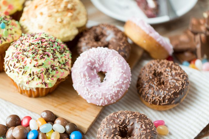 sweet food, junk-food and eating concept - close up of glazed donuts, candies and muffins on wooden board
