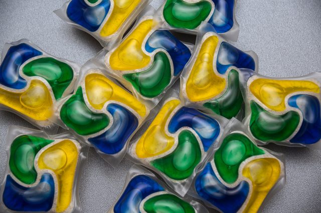 Colorful detergent pods lie scattered on a textured gray surface.
