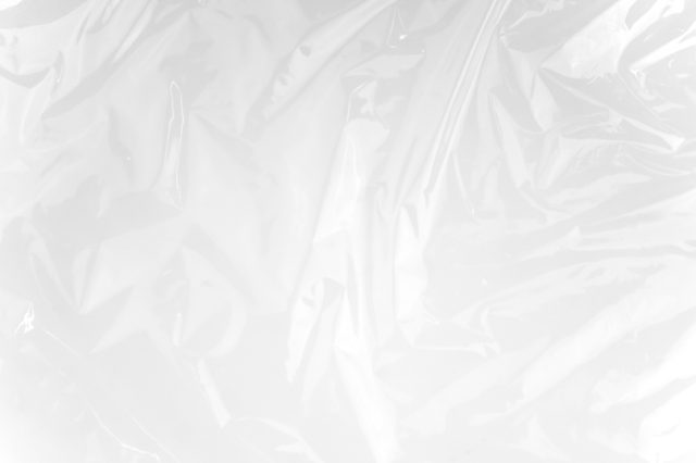 Crumpled transparent plastic sheet lies on a flat surface, creating ripples and folds under soft lighting.