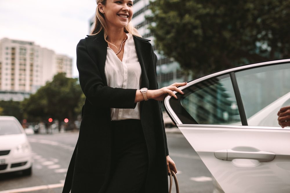 Smiling woman commuter getting out of a taxi. Businesswoman getting off a cab.
