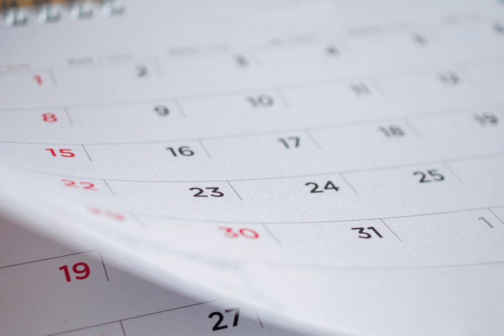 Calendar displaying sequential dates in rows and columns, numbers in black with weekends in red, seen from an angled perspective on a desk.