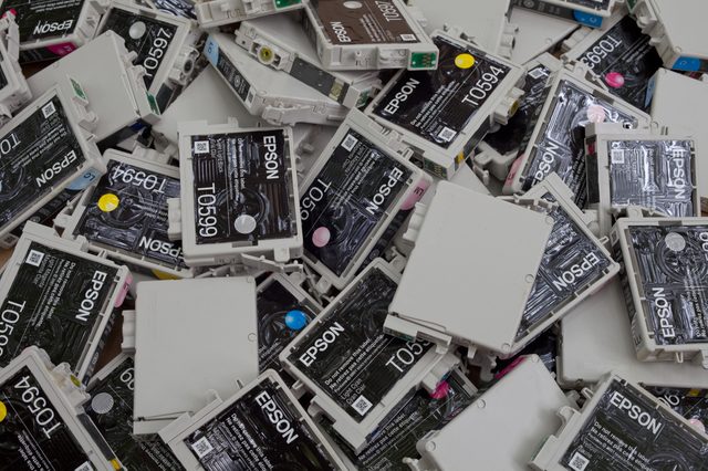 Ink cartridges lie scattered, labeled "EPSON T0599," displaying various colors, forming a piled assortment.