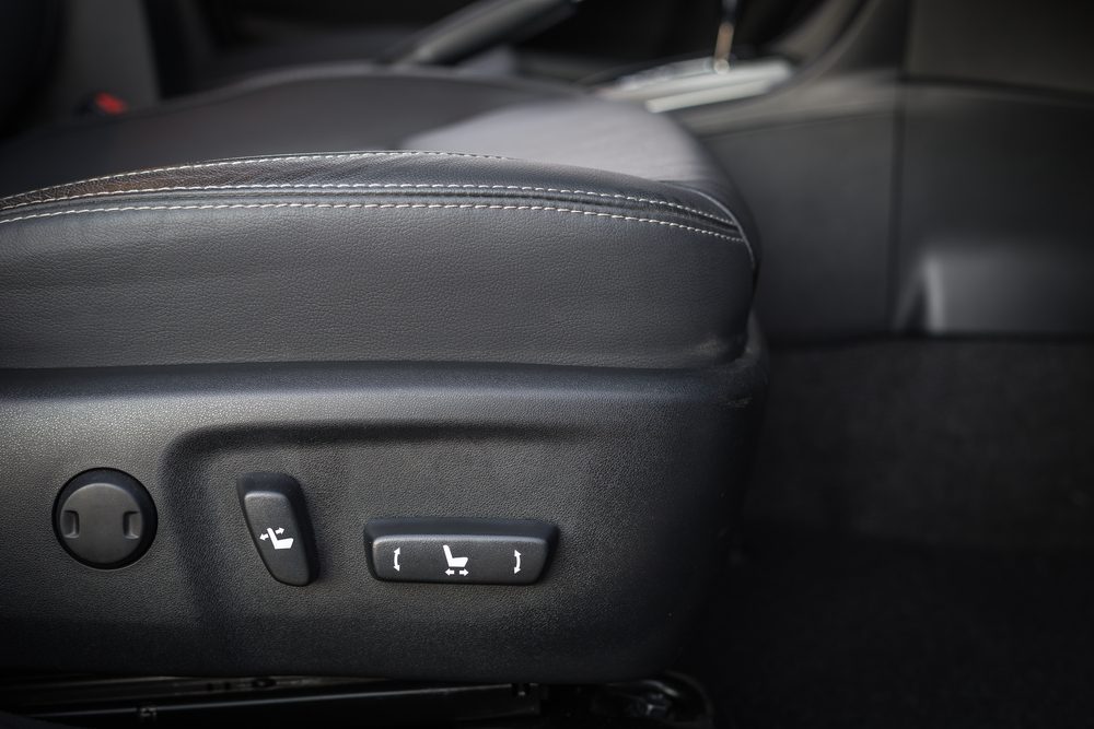 Car seat controls adjust lumbar, backrest position in a dark, leather interior. Buttons are on the side of the seat base.