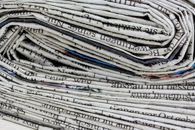 Folded newspapers stacked closely, revealing visible black text in various orientations, creating a layered arrangement.