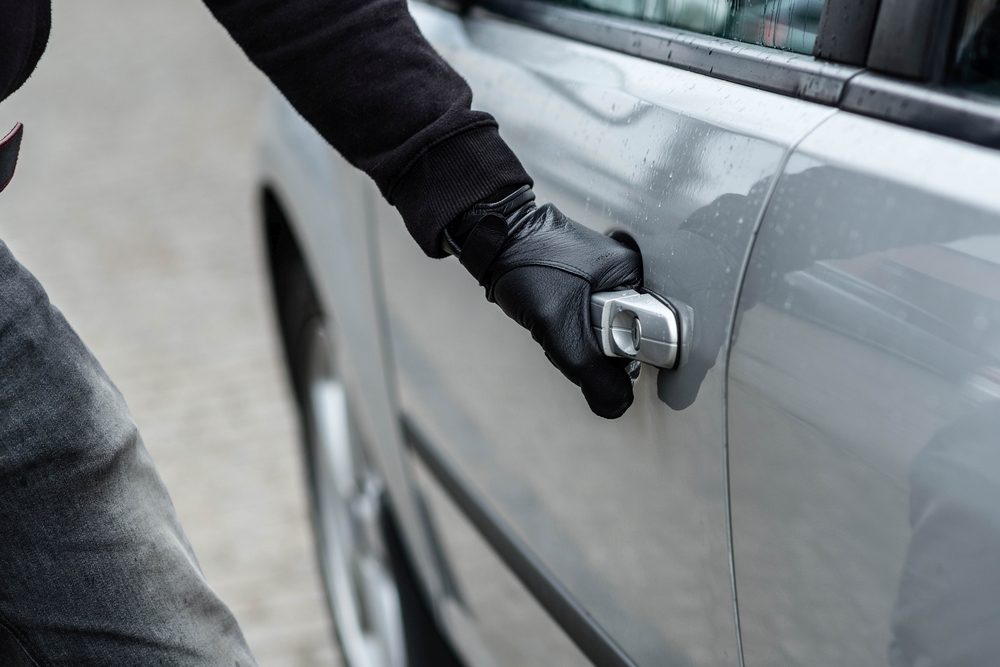 Gloved hand pulling on a car door handle in an outdoor, possibly wet environment.