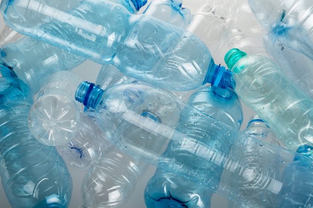 Plastic bottles scattered, overlapping on a surface, some with water droplets, creating a cluttered appearance in a neutral setting.