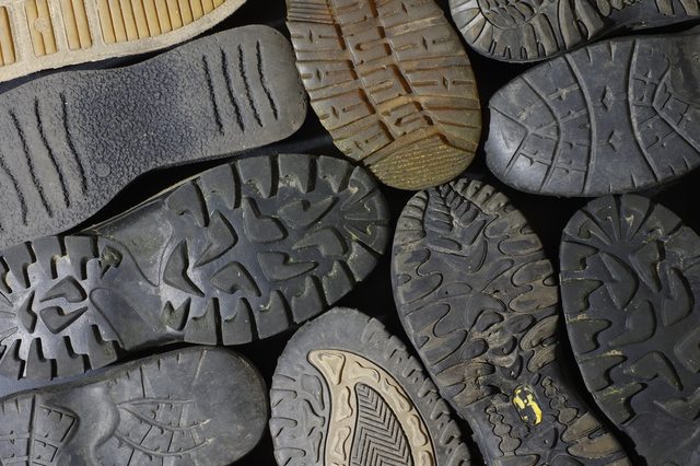 Various shoe soles arranged overlapping, displaying different tread patterns. The soles are scattered on a flat, dark surface.
