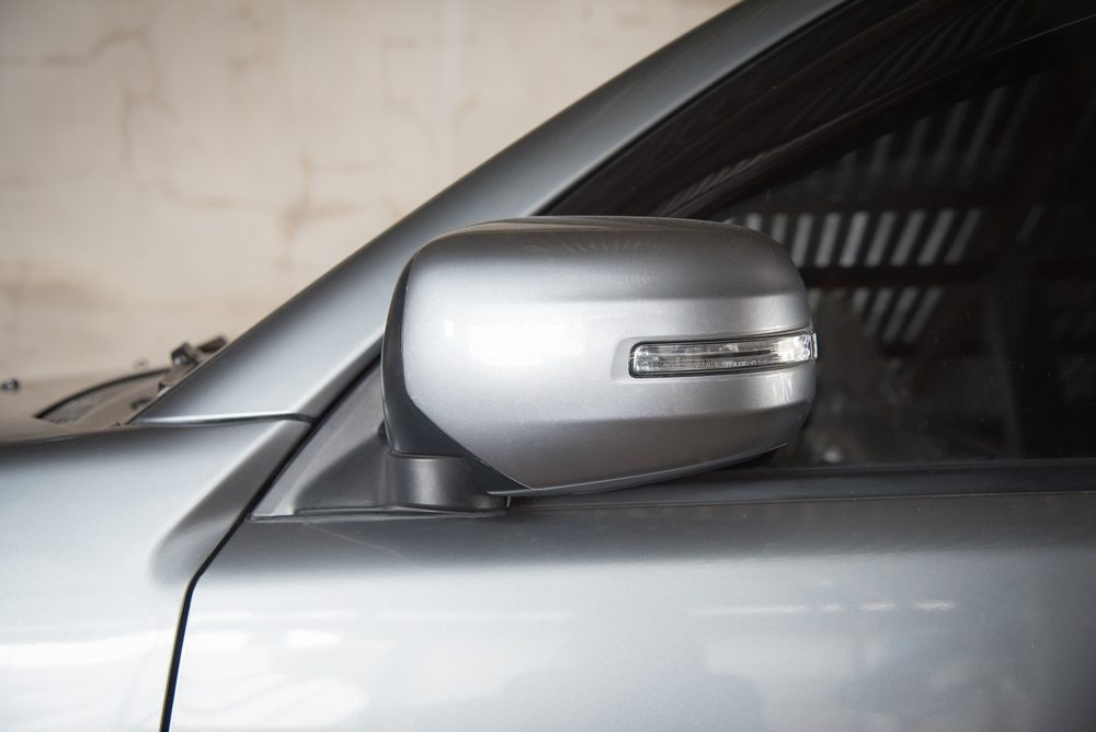 A silver car side mirror with integrated indicator light is attached to the vehicle, located indoors with a neutral background.