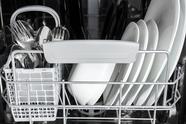 Cutlery and plates are neatly arranged inside a dishwasher rack, which is metallic with a plastic handle.