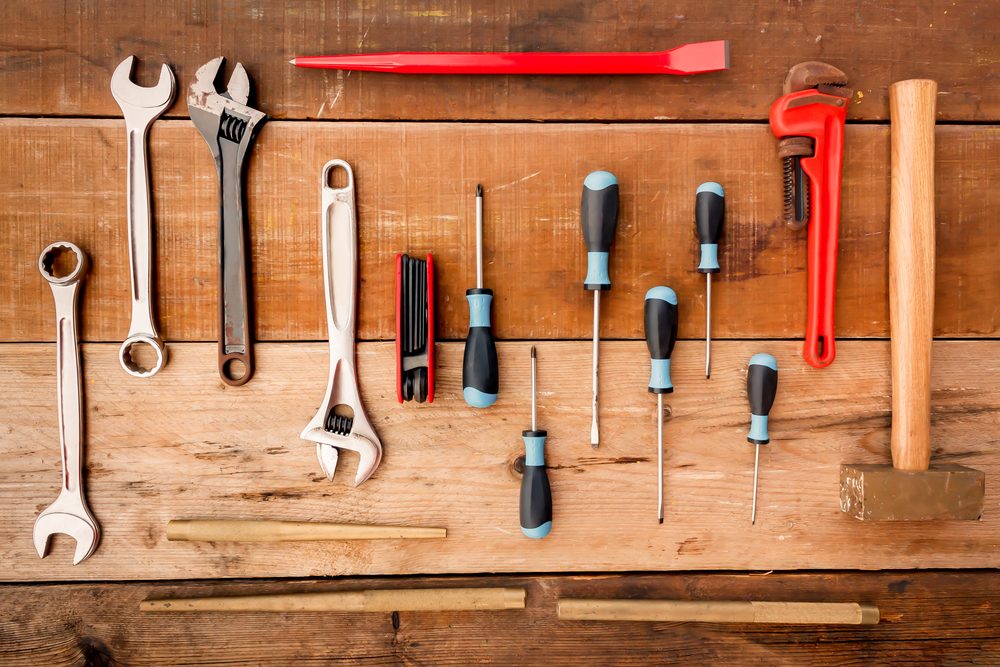 Various tools lie organized on a wooden surface, including wrenches, screwdrivers, a hammer, and a red pry bar, suggesting a workshop setting.