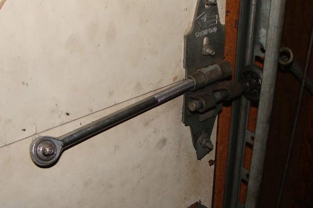 A wrench secures a garage door by tightening onto a bolt. The door is metal, with visible rails and hinges nearby.