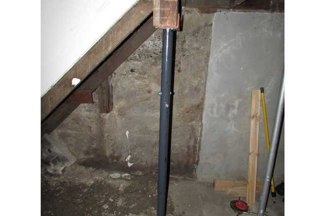 A steel support beam stabilizes a wooden structure within a concrete-walled basement, surrounded by scattered construction tools and materials.