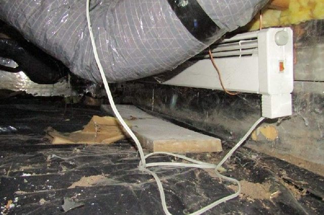 Duct lies connected to a vent, surrounded by wires and insulation in a dusty, cluttered crawlspace.