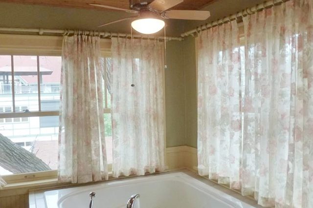 A large bathtub sits beneath floral curtains; a ceiling fan above provides gentle light in a cozy bathroom.