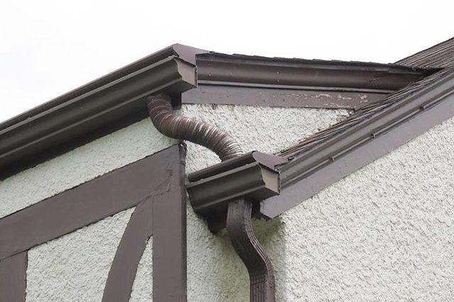 Gutter pipes awkwardly connected on a building corner, showing a mismatch between two sections against a textured wall.