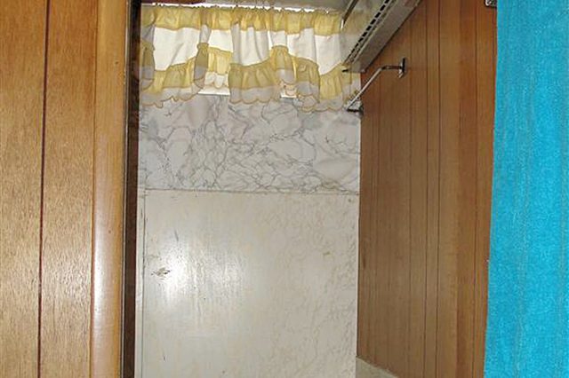 Shower is enclosed by marble-patterned walls, surrounded by wood paneling, with a yellow curtain above. A blue towel hangs on the right wall.