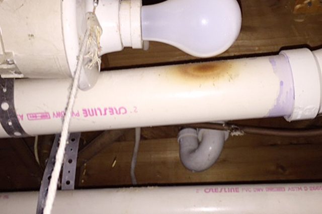 A light bulb with a pull string hangs, surrounded by PVC pipes in a wooden basement ceiling. Text includes "CRESLINE" and "PVC DWV".