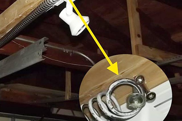 Garage door tension spring mounts near wooden beam, depicted with a close-up inset showing attachment details. Ceiling beams and metal rail visible around.