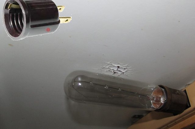Light bulb base points upwards; an adapter floats nearby. The ceiling shows cracked paint, and a shelf is visible below.