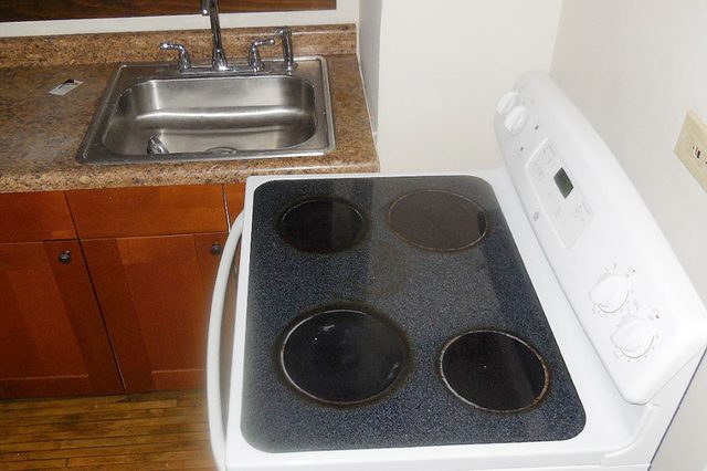 Stove sits idle beside sink in compact kitchen with wooden cabinets and tiled countertop.