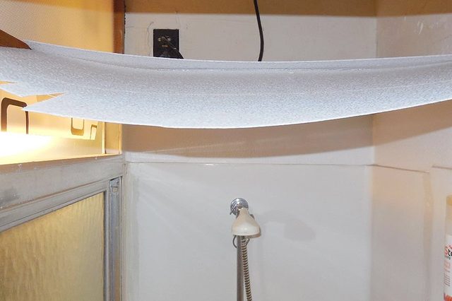 A towel stretches across a shower area from one side to the other, above a handheld shower head attached to a wall.