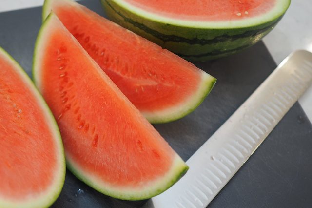 Slices of watermelon, arranged neatly on a cutting board next to a shiny knife, create a fresh, inviting kitchen scene.
