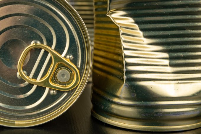 Damaged metal can with vegetables on a wooden table. Canned vegetables in a can. Dark background.