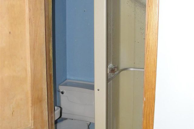 A shower sprays water in a small bathroom; a toilet is adjacent, with walls painted blue.