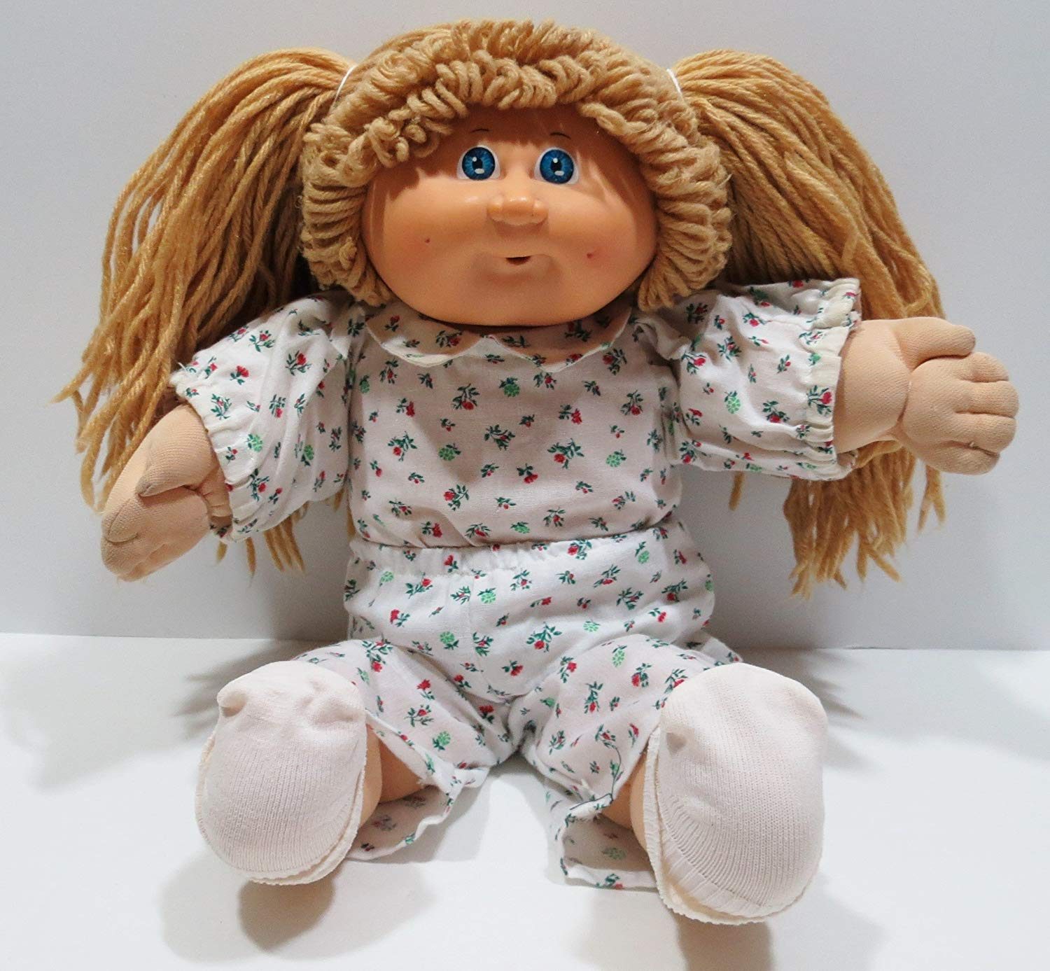 Doll sits wearing floral-patterned pajamas, surrounded by a plain background.