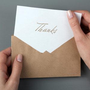 Hands holding an open brown envelope revealing a card with 
