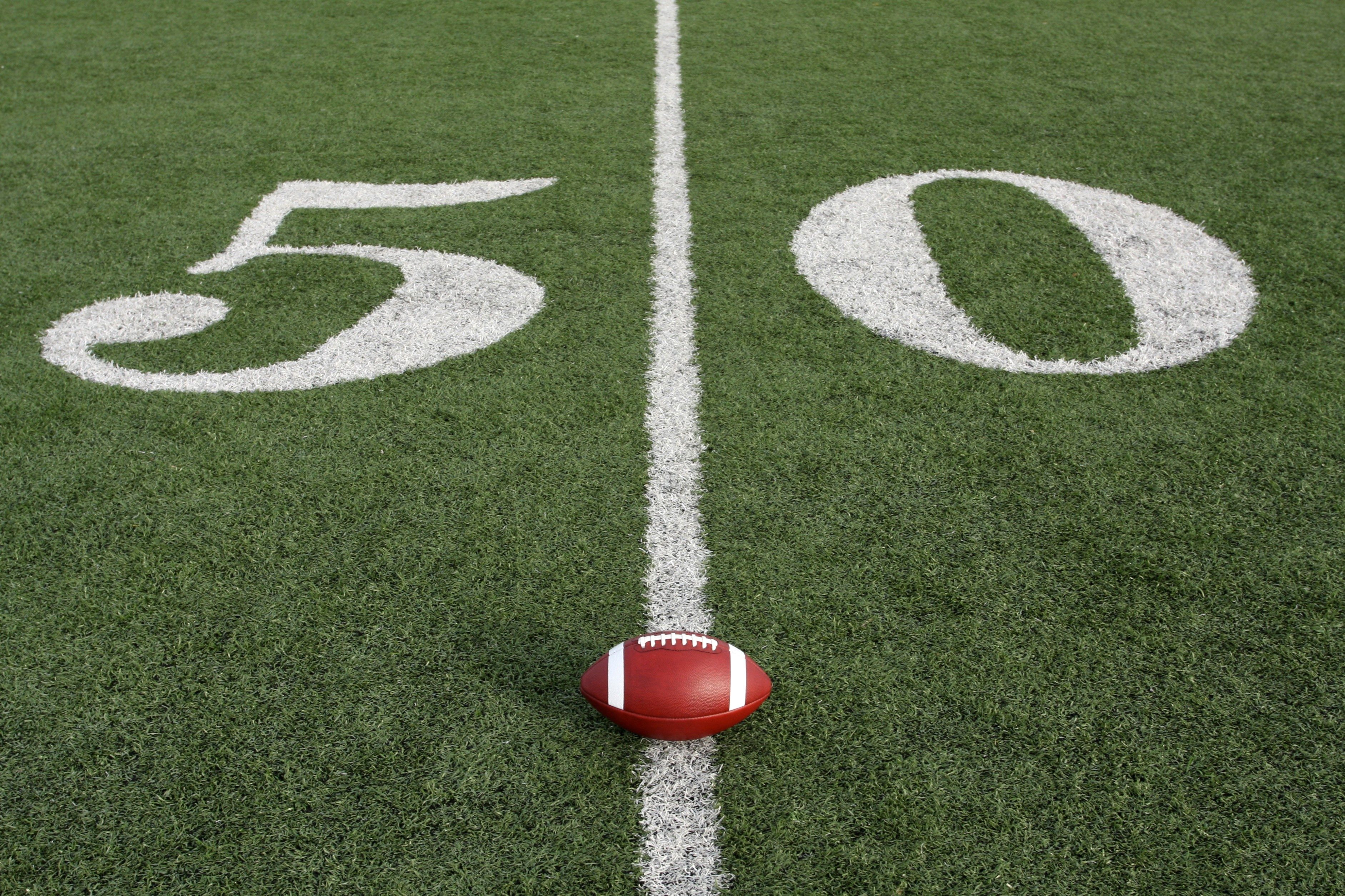 A football rests on the 50-yard line of a grassy field, marked with large white numbers.