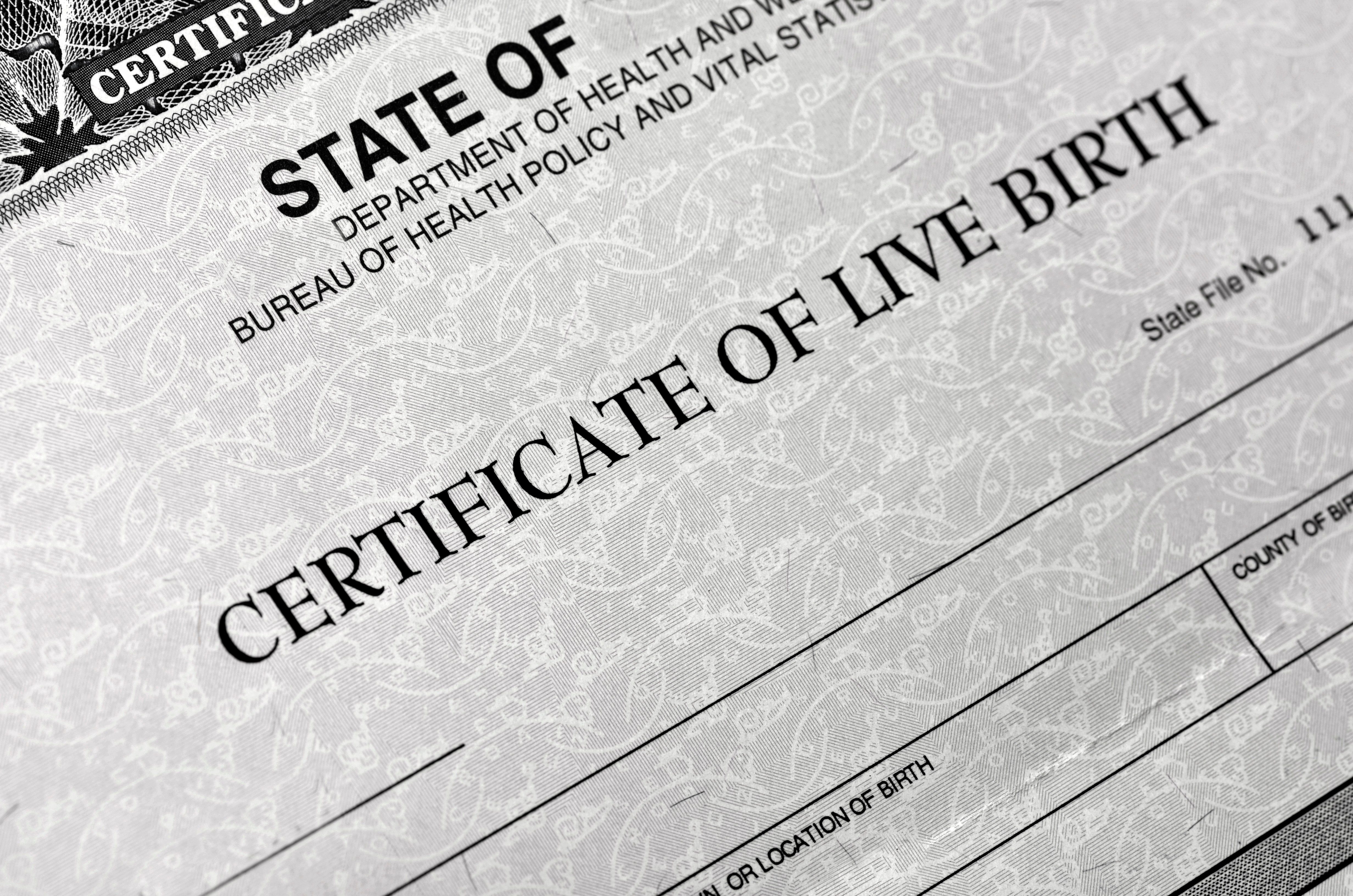 Certificate displays "STATE OF" and "CERTIFICATE OF LIVE BIRTH," set against an ornate, patterned background suitable for official documentation.