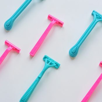 Razors lay arranged in alternating pink and blue diagonals on a plain white background, emphasizing contrast and symmetry.