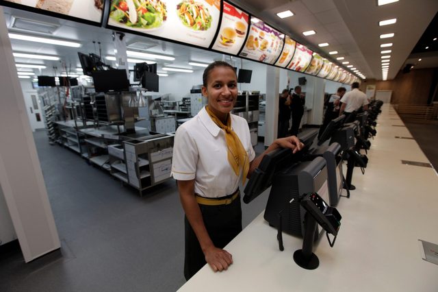 Employee smiles behind counter; displays fast-food restaurant's modern design and digital menu boards.