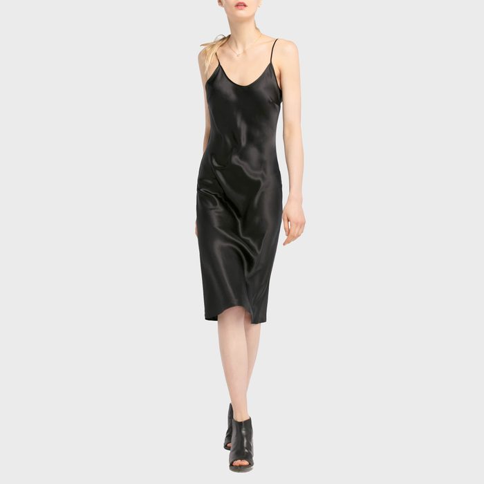 A person models a sleek black slip dress, standing confidently against a plain, neutral background.