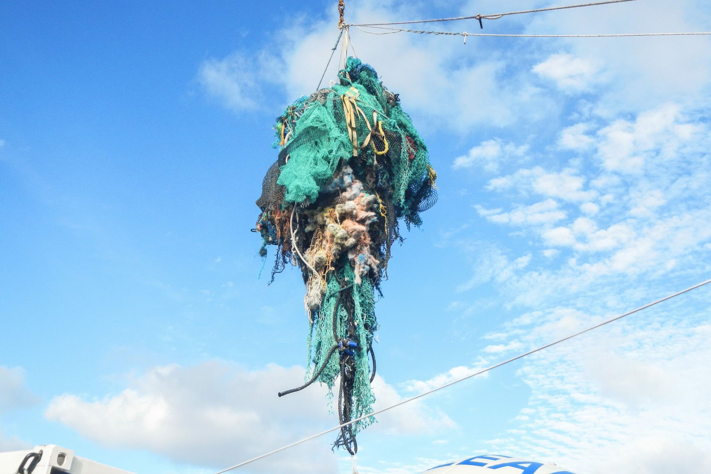 Net bundle hangs from crane, suspended in blue sky backdrop.